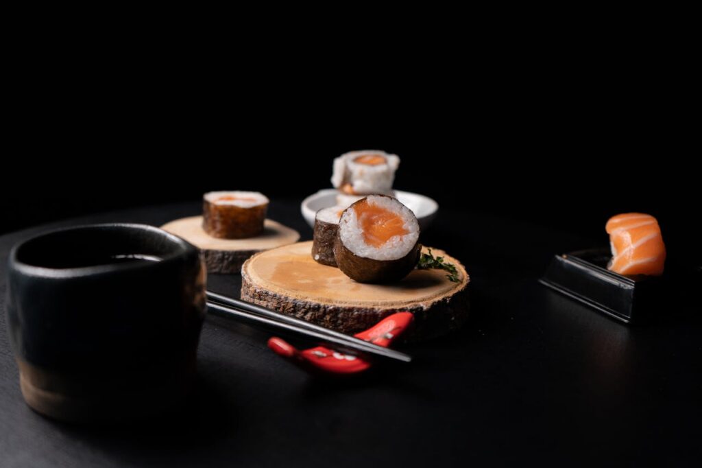 Artistic sushi presentation with rolls and salmon nigiri on a wooden log against a black background.